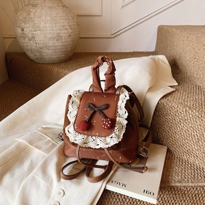 Détail du sac à dos marron enfant avec bordure en dentelle et pendentifs cerises doux
