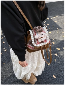 Detalle de mochila infantil marrón con solapa de cuadros, encaje y colgante de perro peluche