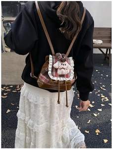 Detalle de mochila infantil de cuero marrón con solapa de cuadros rojos y perrito de peluche