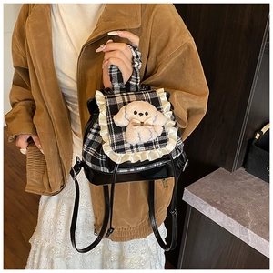 Detalle de mini mochila de cuadros para niños con perrito de peluche y ribete de encaje blanco