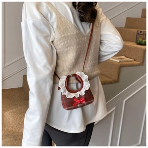 Detail of a mini plaid crossbody bag with lace-wrapped handle and red sequin bow