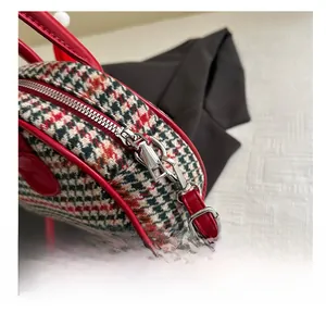 Détail de la fermeture éclair argentée et du passepoil rouge sur le sac en tweed
