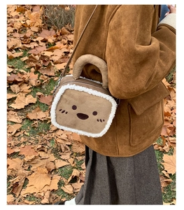 Close-up of toast-shaped brown suede shoulder bag with white fleece trim and smiley face