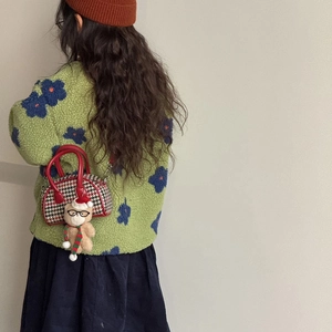 Détail d'un sac à main pied-de-poule rouge avec ours en peluche sur manteau polaire vert