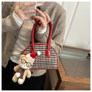 Detail of red houndstooth shell bag with a cute plush bear charm held by a model