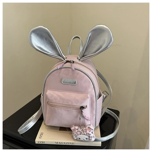 Detailed view of pink rabbit-eared backpack featuring metal logo and fuzzy cat charm