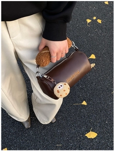 Detail of a brown cylinder bag with plush handle and cute cookie pendant accessory