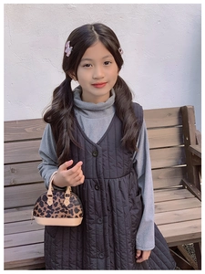 Kleinkind in grauem Strick und Steppweste mit einer Mini-Muscheltasche im Leopardenmuster