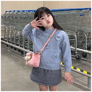 Maglione bimba blu con pompon a cuore e borsa a tracolla rosa tra carrelli della spesa