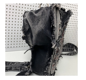 Detail of dark gray washed denim bag with frayed edges and red embroidery stitching