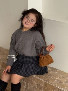 Dettaglio di cardigan grigio in maglia e gonna scozzese per bambini con borsa marrone piccola