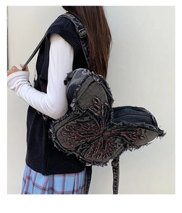 Detail of butterfly denim crossbody bag with distressed edges and red wing embroidery