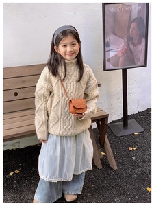 Detailed texture of kids' cream cable-knit sweater with orange woven crossbody bag