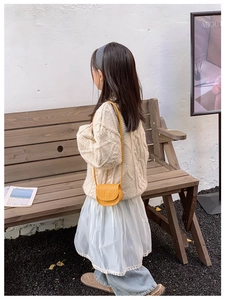 Detailed view of yellow woven mini crossbody bag on a child in a cozy knit outfit