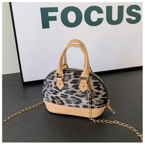 Detail der Mini-Muscheltasche mit Leopardenmuster und goldener Kette auf schwarzem Holz