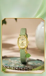 Detail view of oval gold watch with green fan charm and sunray dial for women