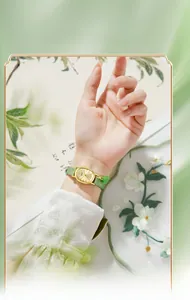 Close-up of golden oval watch with green strap and emerald charm on a silk background
