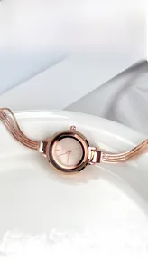 Close-up of rose gold bracelet watch with diamond accents and tassel-style metal chains