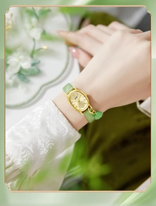 Detail of vintage oval gold watch with green leather strap and floral charm on wrist