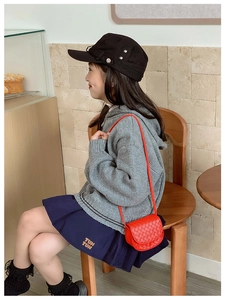Kid's red quilted crossbody bag shown with grey hoodie and pleated skirt outfit