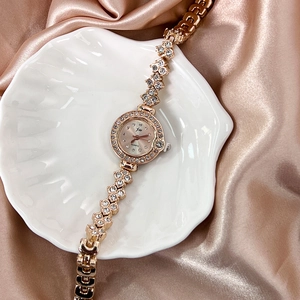 Gros plan d'une montre bijou or rose sertie de strass sur coquillage et soie blanche
