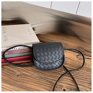 Detail of black woven leather mini crossbody bag for kids on a rustic wooden table