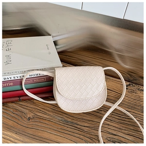 Close-up of cream woven mini crossbody bag for kids on a wooden table with books