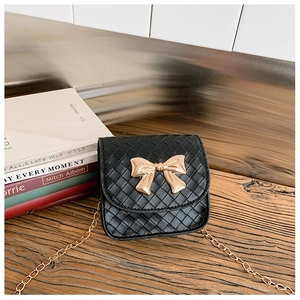 Détail de la texture tressée du sac bandoulière noir avec fermoir nœud doré sur bois