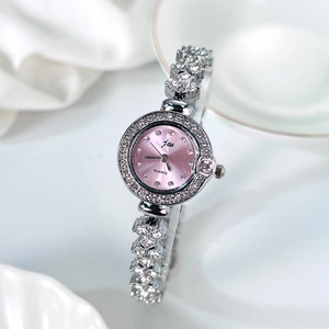 Détail d'une montre à quartz avec cadran rose et bracelet serti sur un tissu blanc