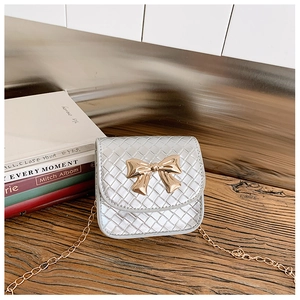 Gros plan du mini sac argenté tressé avec fermoir nœud doré sur table en bois