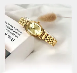 Close-up of golden oval watch with metal chain strap on white fabric and flowers