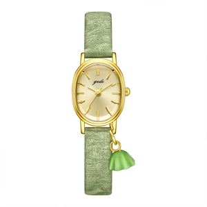 Elegant gold oval watch with light green textured strap and floral charm pendant
