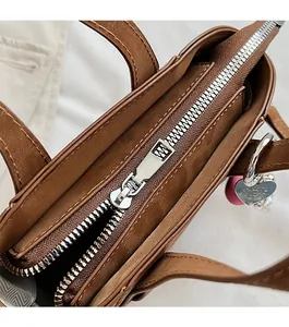 Detail view of a brown leather handbag with smooth zipper and silver heart charm