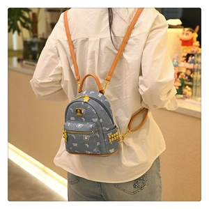 Detail of light blue denim backpack featuring white bear prints and gold rivet accents