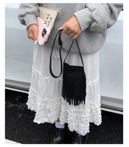 Détail d'un mini sac bandoulière noir à franges porté par un mannequin en style décontracté