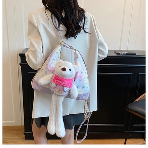 Close-up of plush white bear charm on purple pattern crossbody bag with chain strap