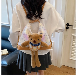 Close-up of white printed shoulder bag featuring a cute plush bear and gold chain strap