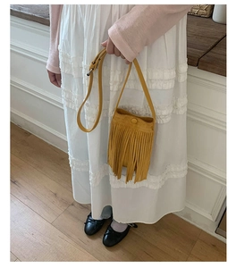 Détail d'un sac seau jaune à franges bohèmes porté par un mannequin en robe blanche