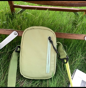 Detail of light green nylon crossbody bag with vertical zipper on lush grass
