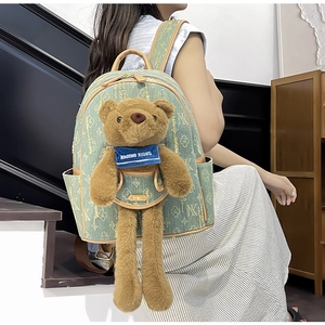 Detail of light green denim backpack with plush bear charm and clover pattern