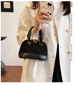 Detail of mini black quilted shell handbag with gold zippers held by a woman in a trench coat