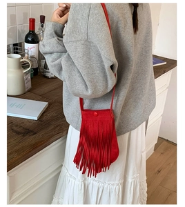 Petit sac seau rouge à franges porté en bandoulière sur un sweat-shirt gris