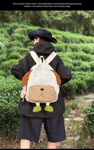 Detail of cute puppy-shaped backpack with brown ears and green charms on the model's back