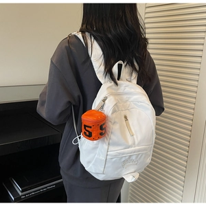 Detail of white mini backpack featuring an orange heart-shaped charm and embroidery