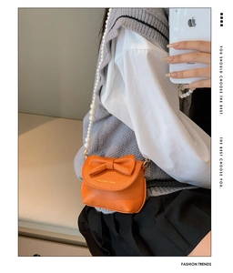 Detail view of mini orange crossbody bag with large bow and pearl metal chain strap