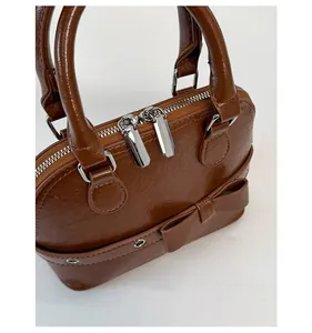 Detail of glossy brown shell bag with dual silver metal zippers and bow decoration