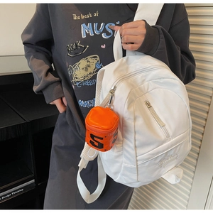 Close-up of white minimalist backpack with glossy orange heart-shaped mini coin purse