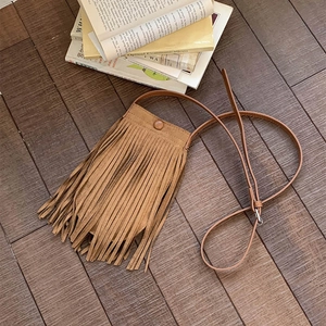 Détail du sac à bandoulière en PU mat marron avec franges sur fond de parquet en bois rustique