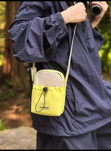 Detail of yellow and white crossbody phone bag with drawstring on a blue jacket
