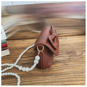 Detail of a mini brown leather crossbody bag featuring a bow and pearl strap